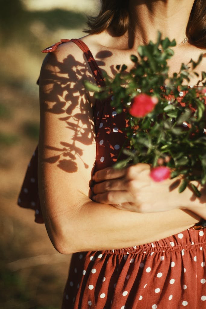 A woman in a polka dot dress holding flowers with beautiful shadow play in sunlight.