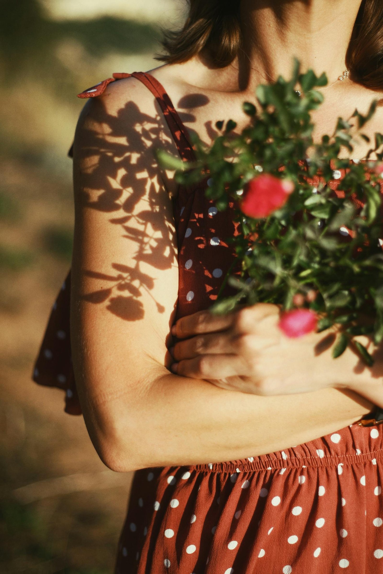 A woman in a polka dot dress holding flowers with beautiful shadow play in sunlight.